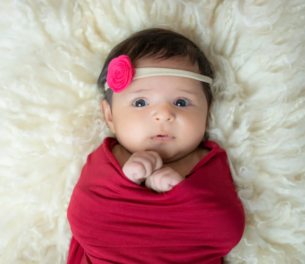 Serene newborn photography in Ahmedabad with a baby swaddled in maroon on a white crib.