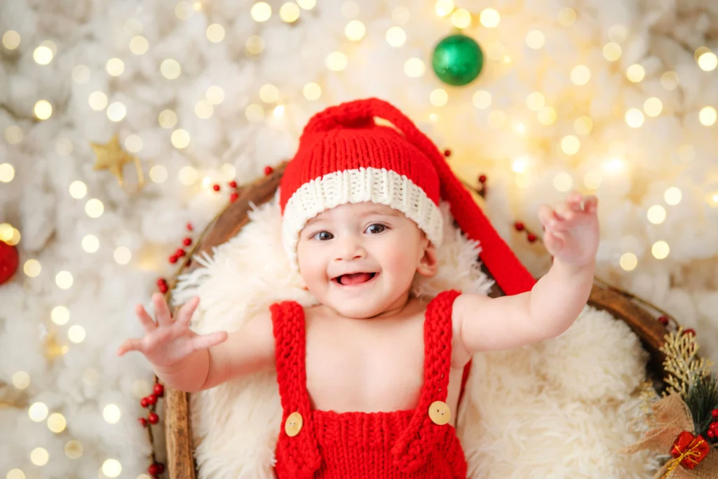 Happy baby in a red Santa hat in a bright photoshoot, saving sweet memories in Ahmedabad.