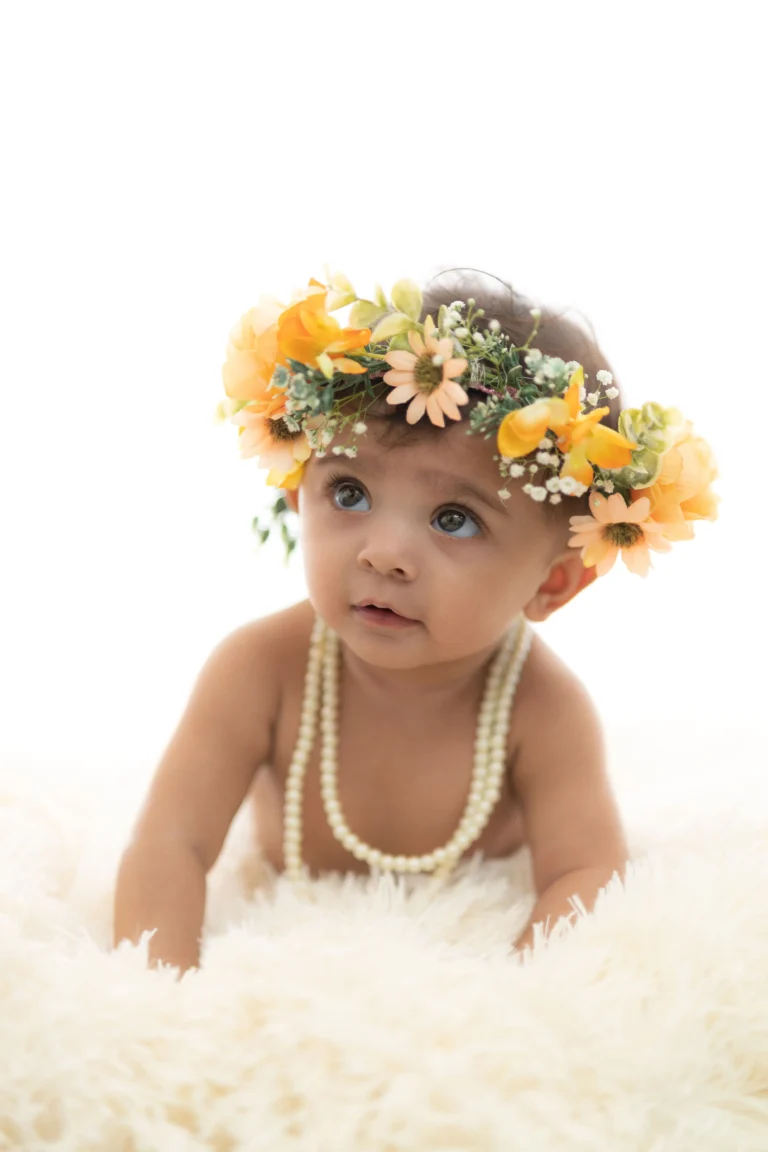 Curious newborn with a floral headband gazing gently, captured in a natural light photoshoot.