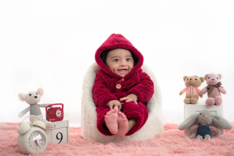 Cheerful newborn in a vibrant red outfit smiling for a festive photoshoot moment.