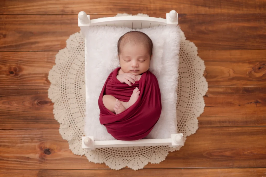 Maroon-swaddled newborn captured in a serene moment, showcasing the art of newborn photography in Ahmedabad.