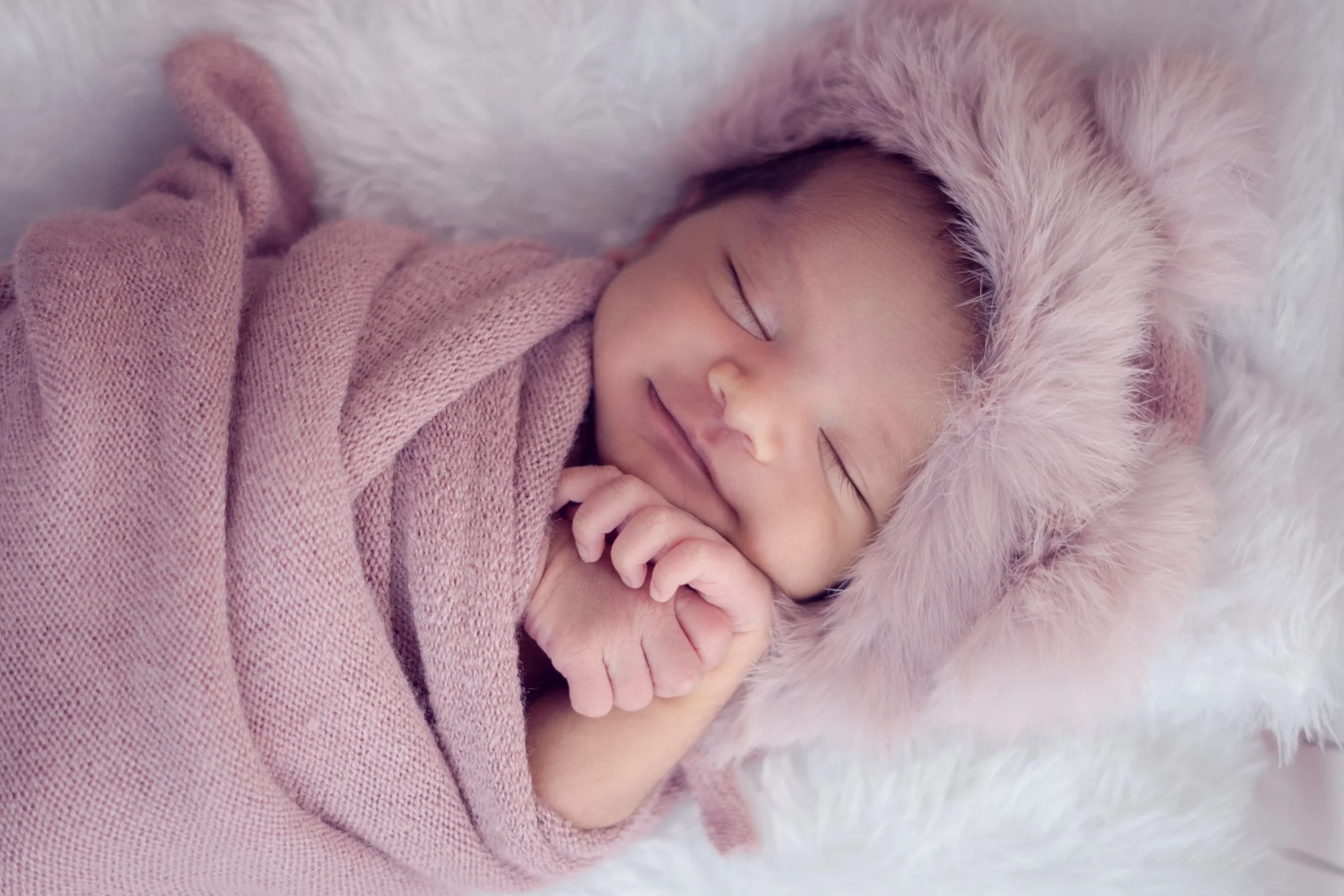 Newborn baby smiling in peaceful sleep, wrapped in a pink blanket for a cozy newborn photoshoot in Ahmedabad.