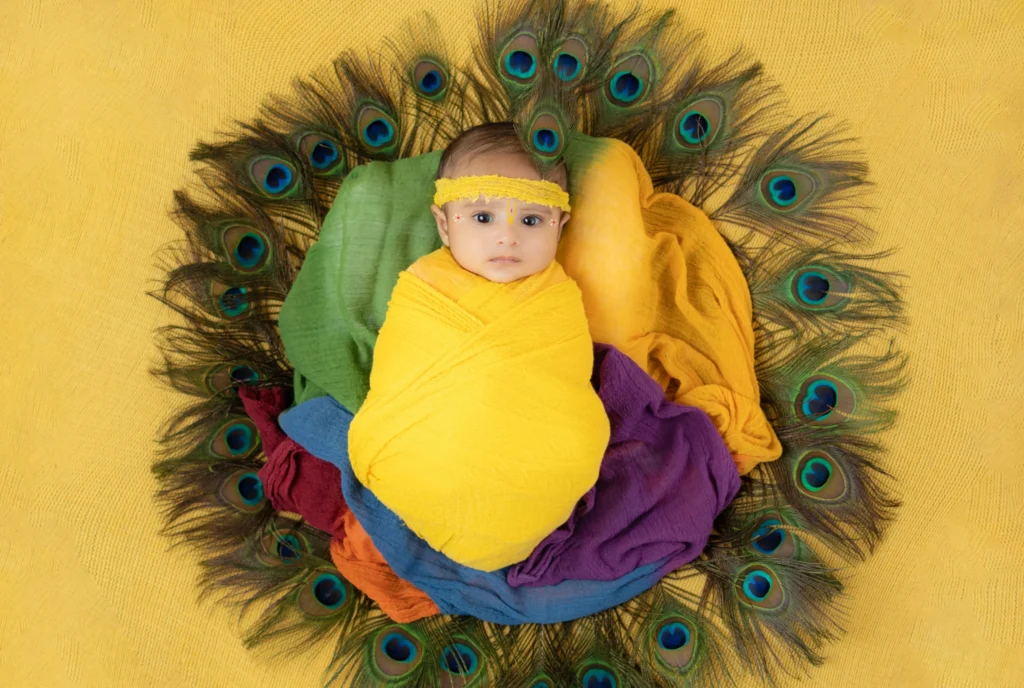 Newborn enveloped in vibrant colors with peacock feathers during a themed photoshoot in Ahmedabad.